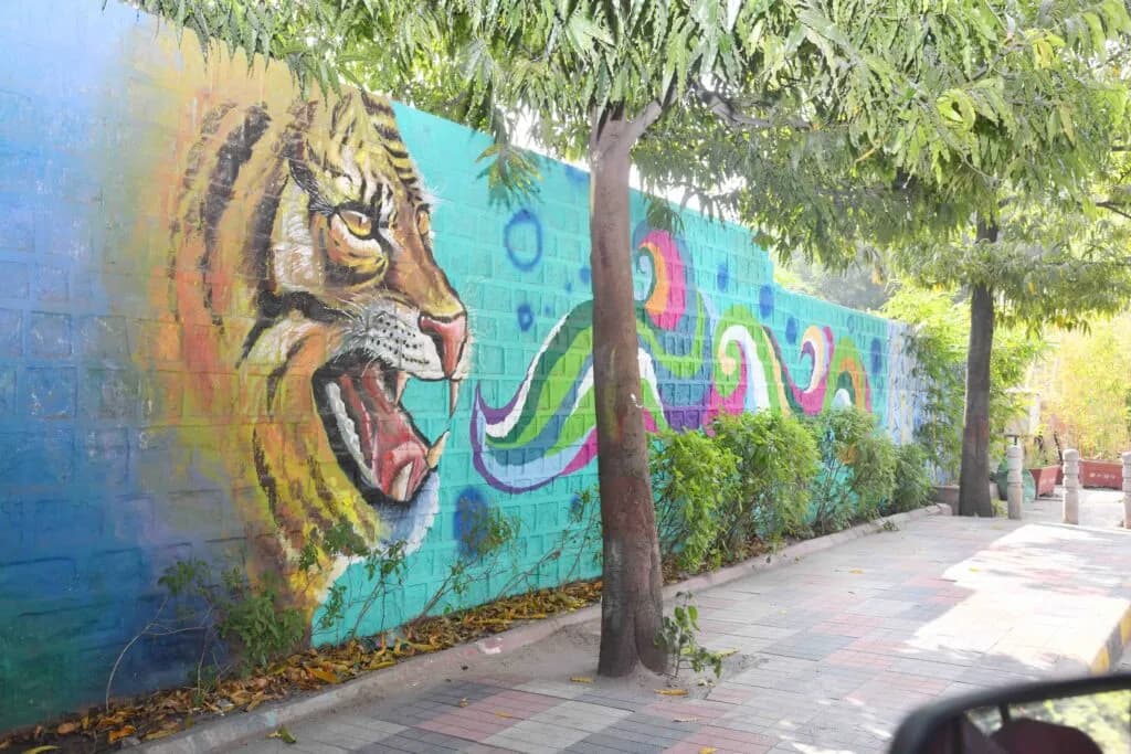 Wall mural of a roaring tiger in orange and blue beside a tree-lined path