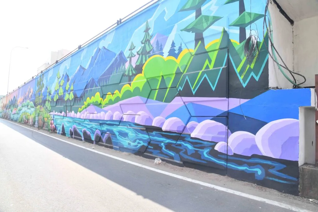 Long roadside wall mural of stylised mountains, trees and water in blue and green