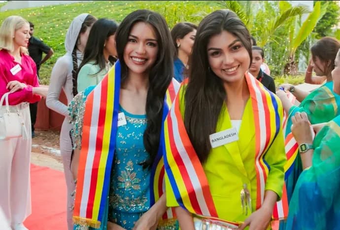 Two women wearing sashes smiling outdoors with a group standing behind them