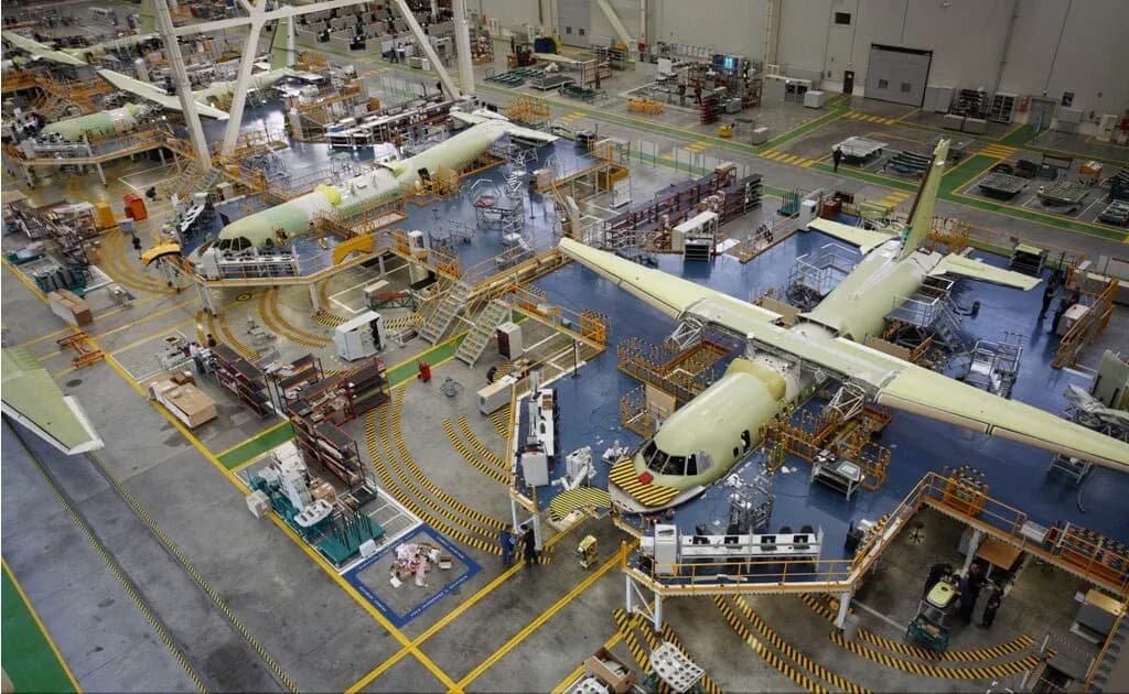 Aircraft under assembly inside a large industrial hangar with overhead gantries
