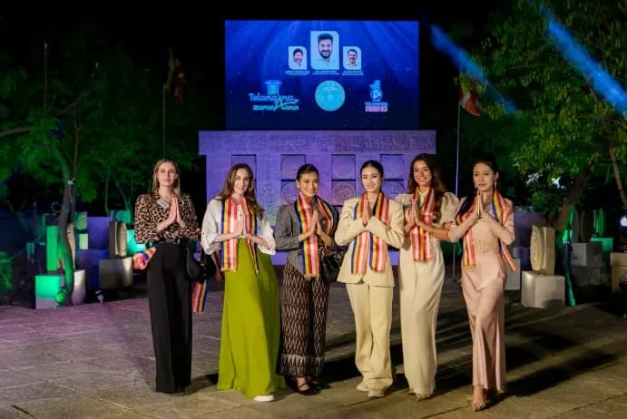 Six women in sashes standing together on an outdoor stage at night