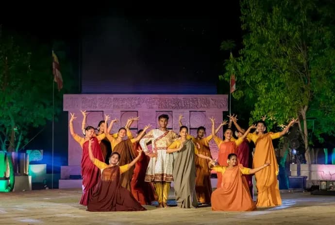 Dancers in red and orange costumes performing on an outdoor stage at night