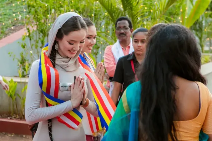 Women in sashes greeting people with folded hands at an outdoor gathering