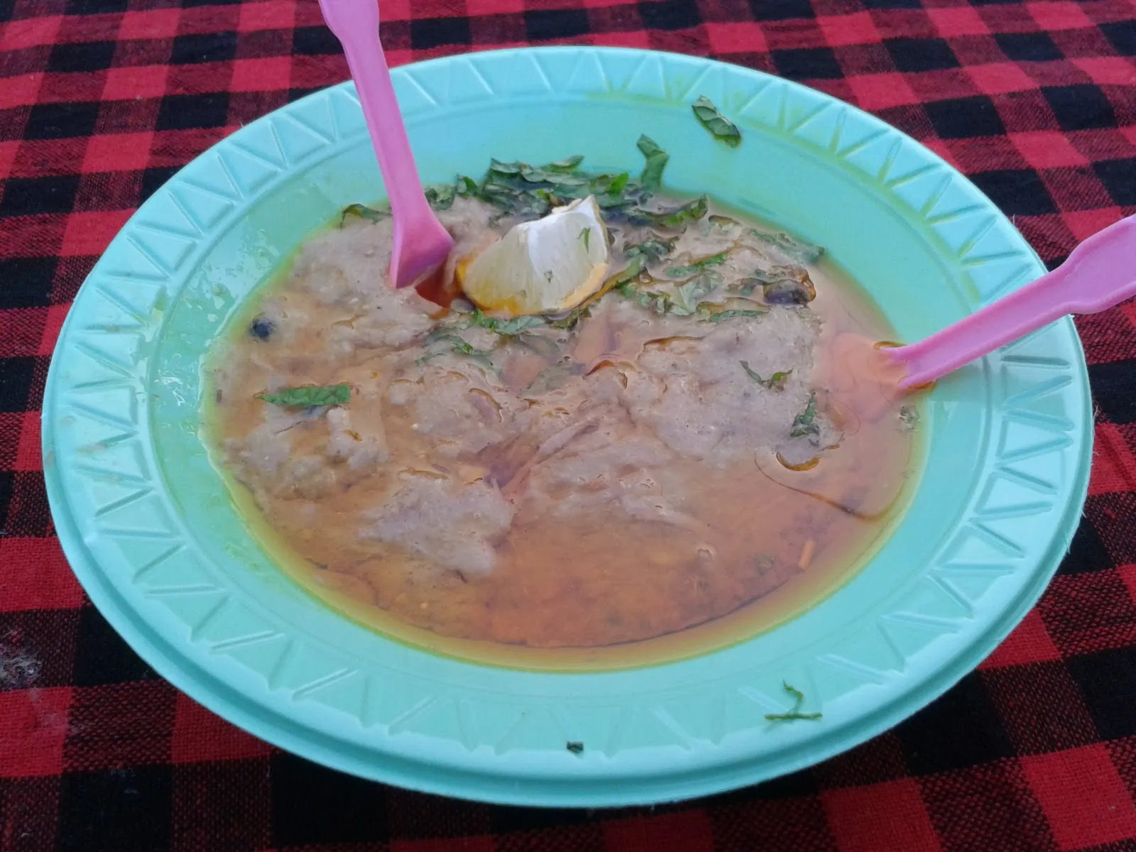 Bowl of thick stew with a spoon on a green plate over a checked cloth