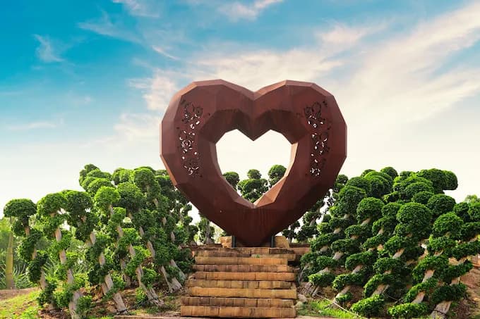 Large heart-shaped stone sculpture on steps surrounded by clipped shrubs