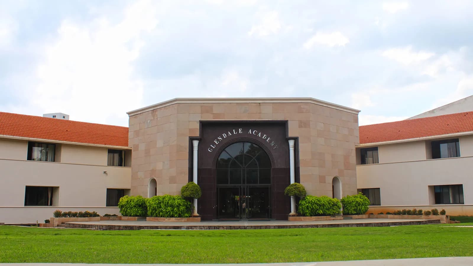 Low sandstone institutional building with a lawn and clipped hedges in front