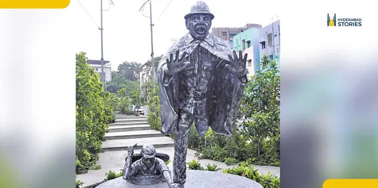 Bronze statue of a standing figure on a plinth in a landscaped garden