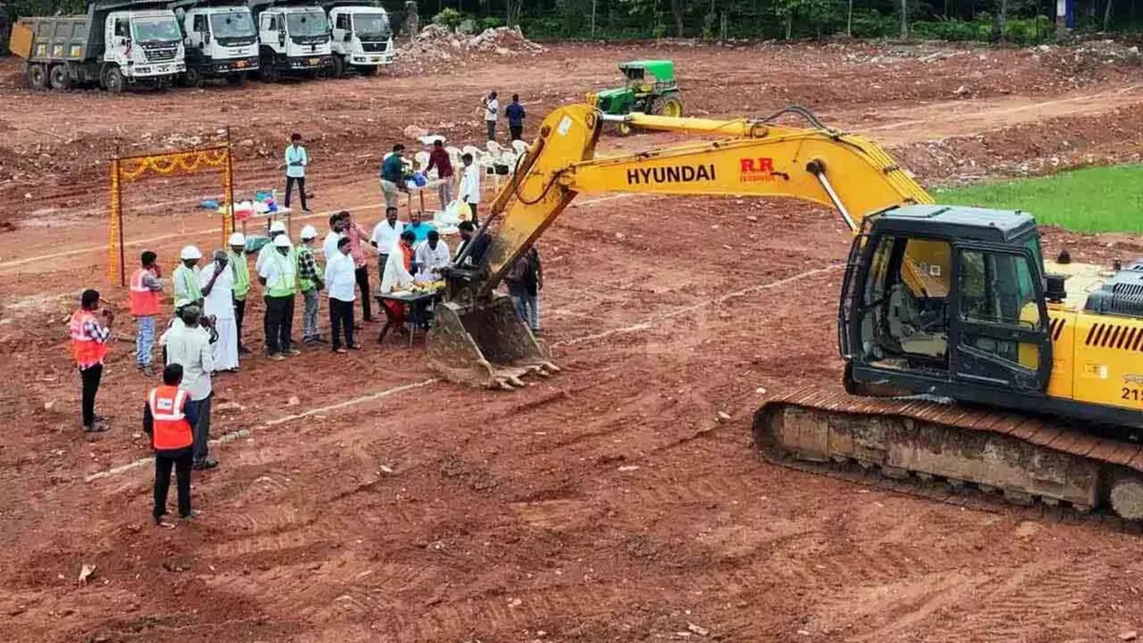 Aerial view of an excavator and a crowd at a groundbreaking on bare ground
