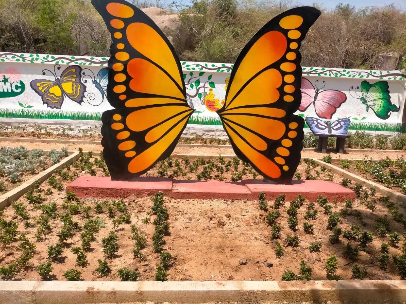 Large orange butterfly sculpture in a planted bed beside a painted wall