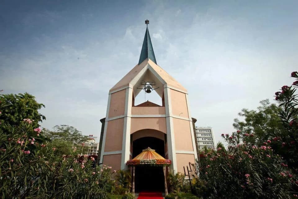 White church with a steeple and bell set among flowering shrubs