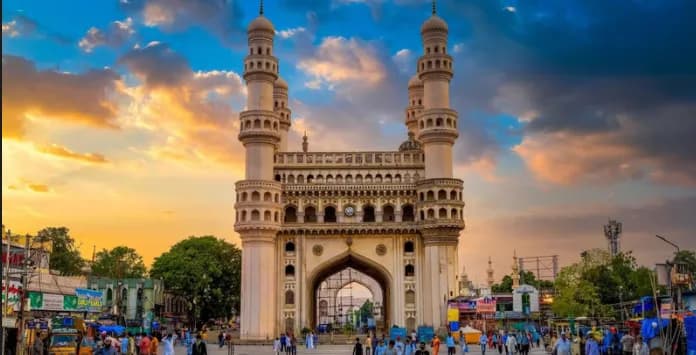 Four-minaret stone monument at sunset above a busy street
