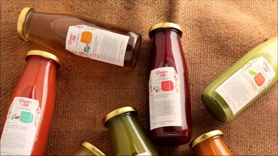 Glass bottles of coloured juices with printed labels arranged on brown cloth