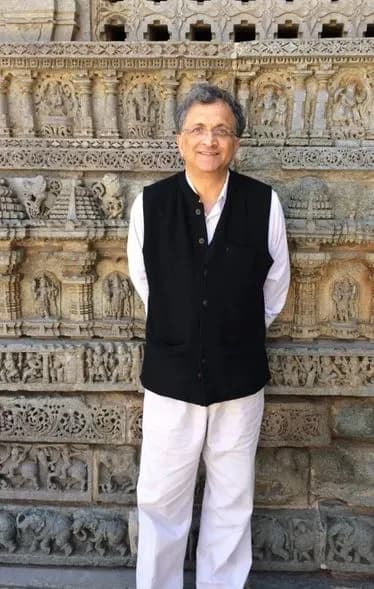 Man in a dark waistcoat standing before a carved stone temple wall