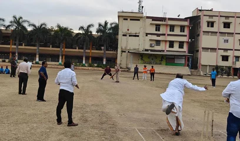 Students playing cricket on a dirt ground beside a school building