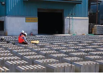 Rows of stacked white bricks drying outside an industrial shed