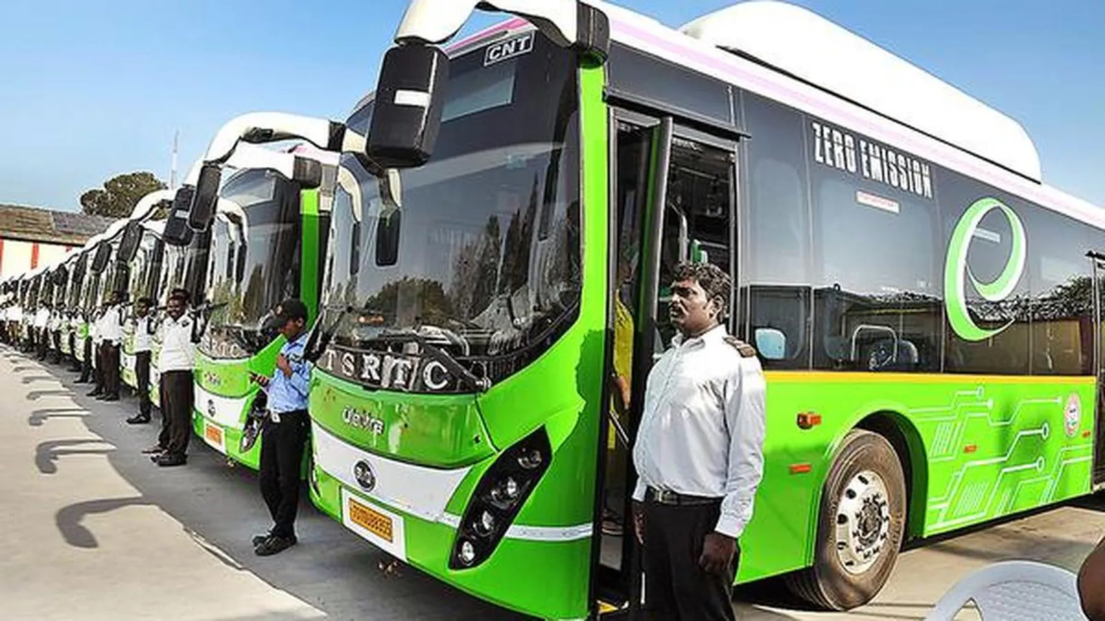 Row of green electric buses parked with drivers standing beside them
