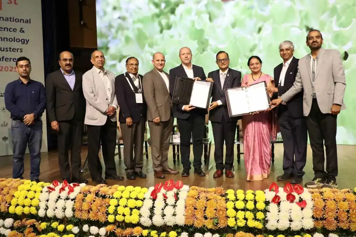 Group on a stage holding framed certificates behind floral garlands