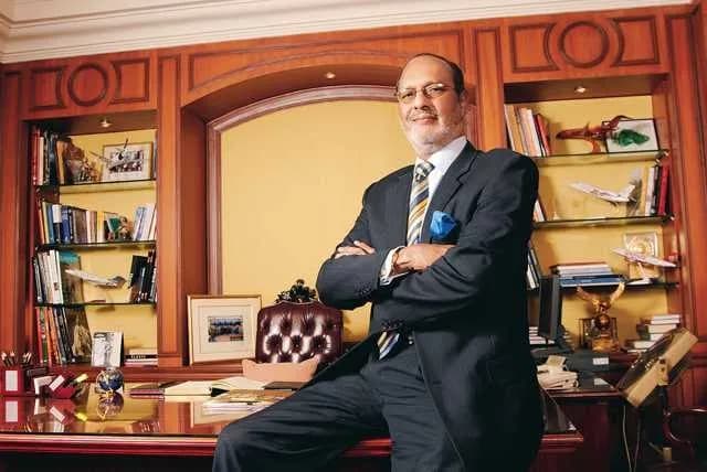 Man in a suit leaning against a desk in a wood-panelled room lined with books