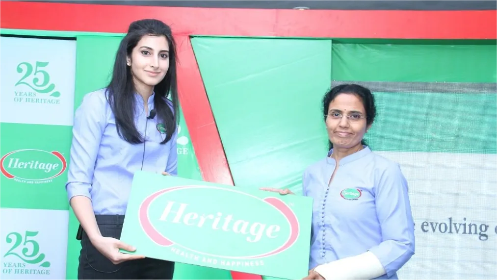 Two people in uniform holding a branded sign at a promotional stand