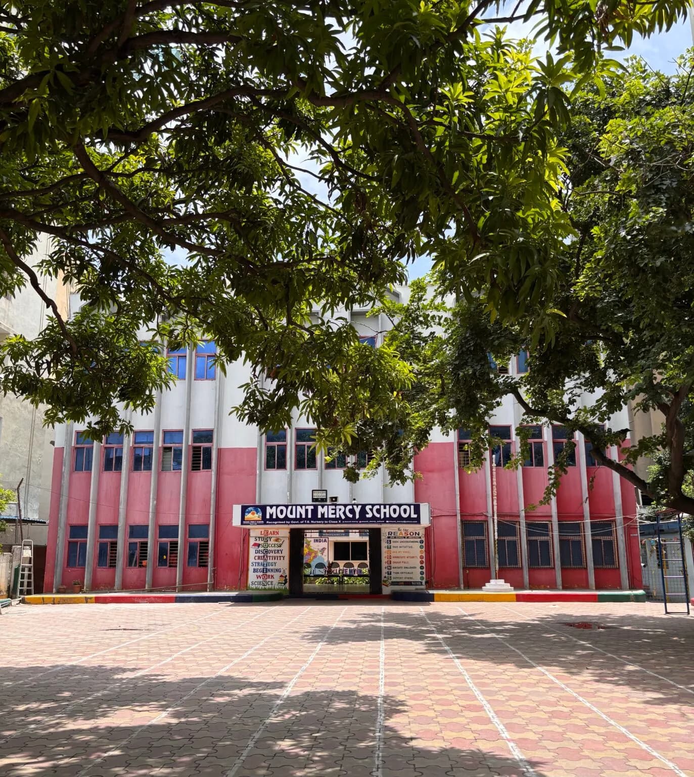School building behind a bare playground and large tree