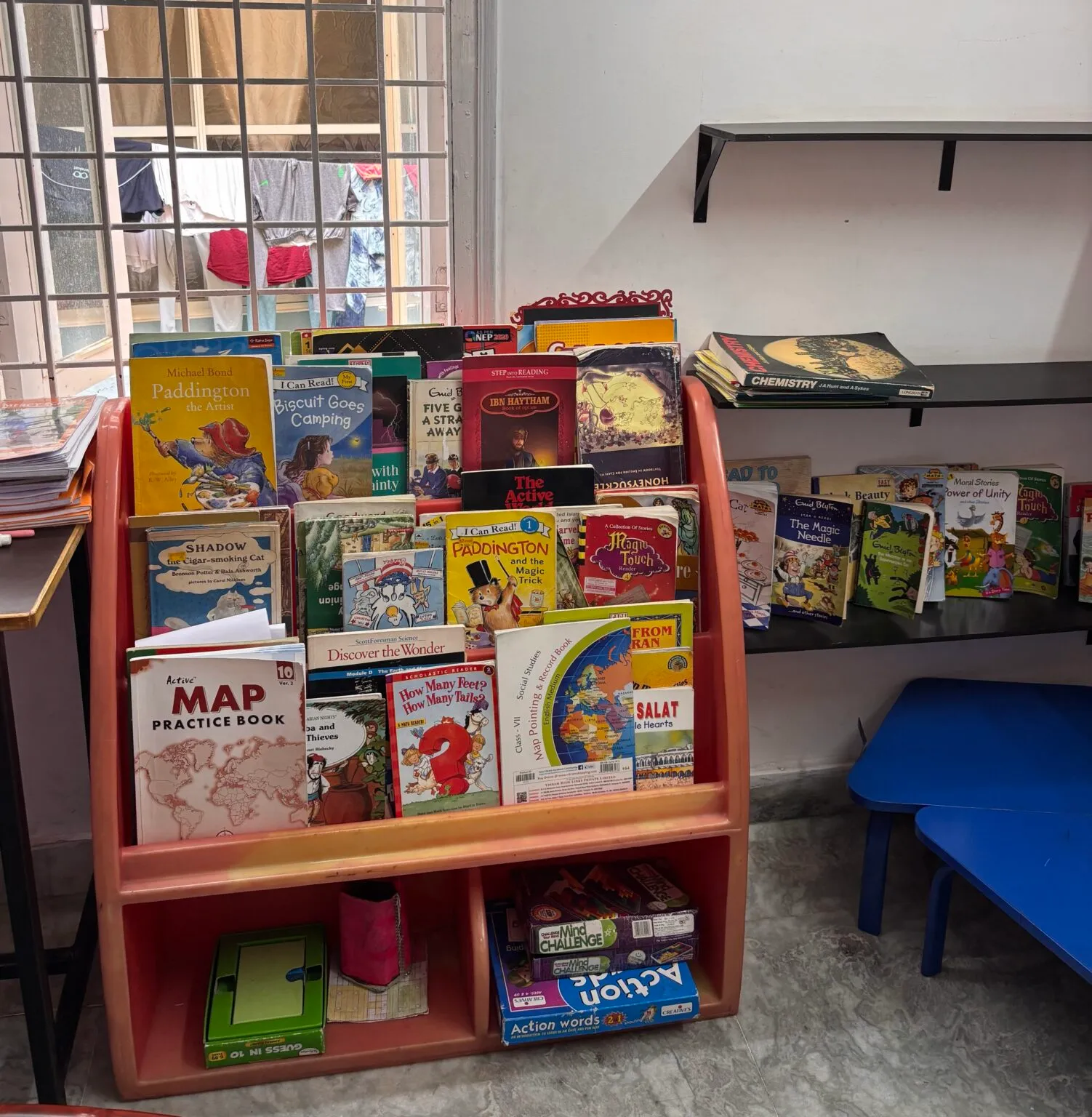 Wooden rack of children's books beside a blue bench