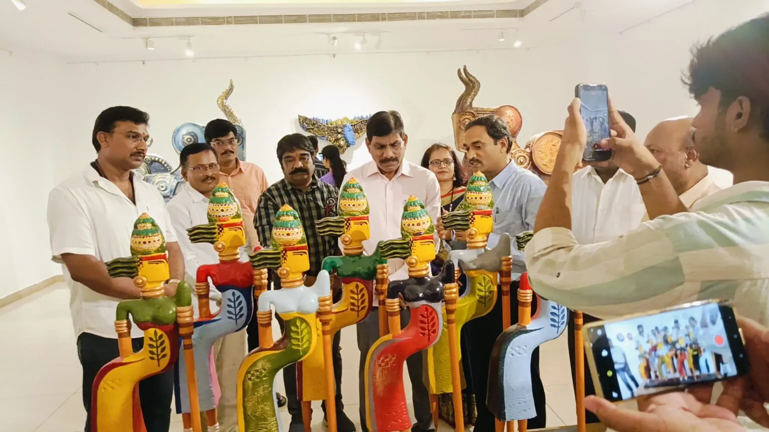 People holding painted wooden figures at an exhibition