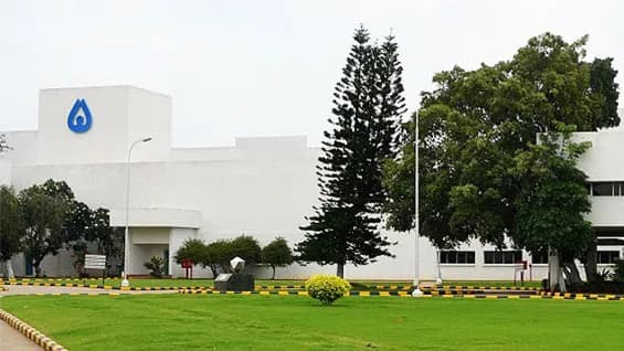 Low white industrial building set behind a lawn and tall trees
