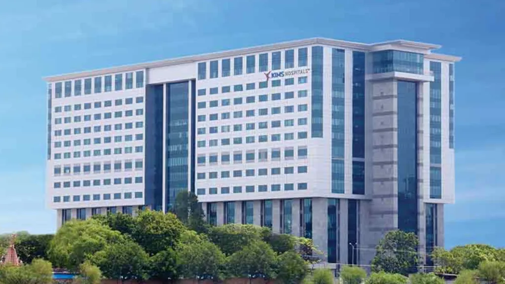Multi-storey hospital building with rows of windows, seen behind trees