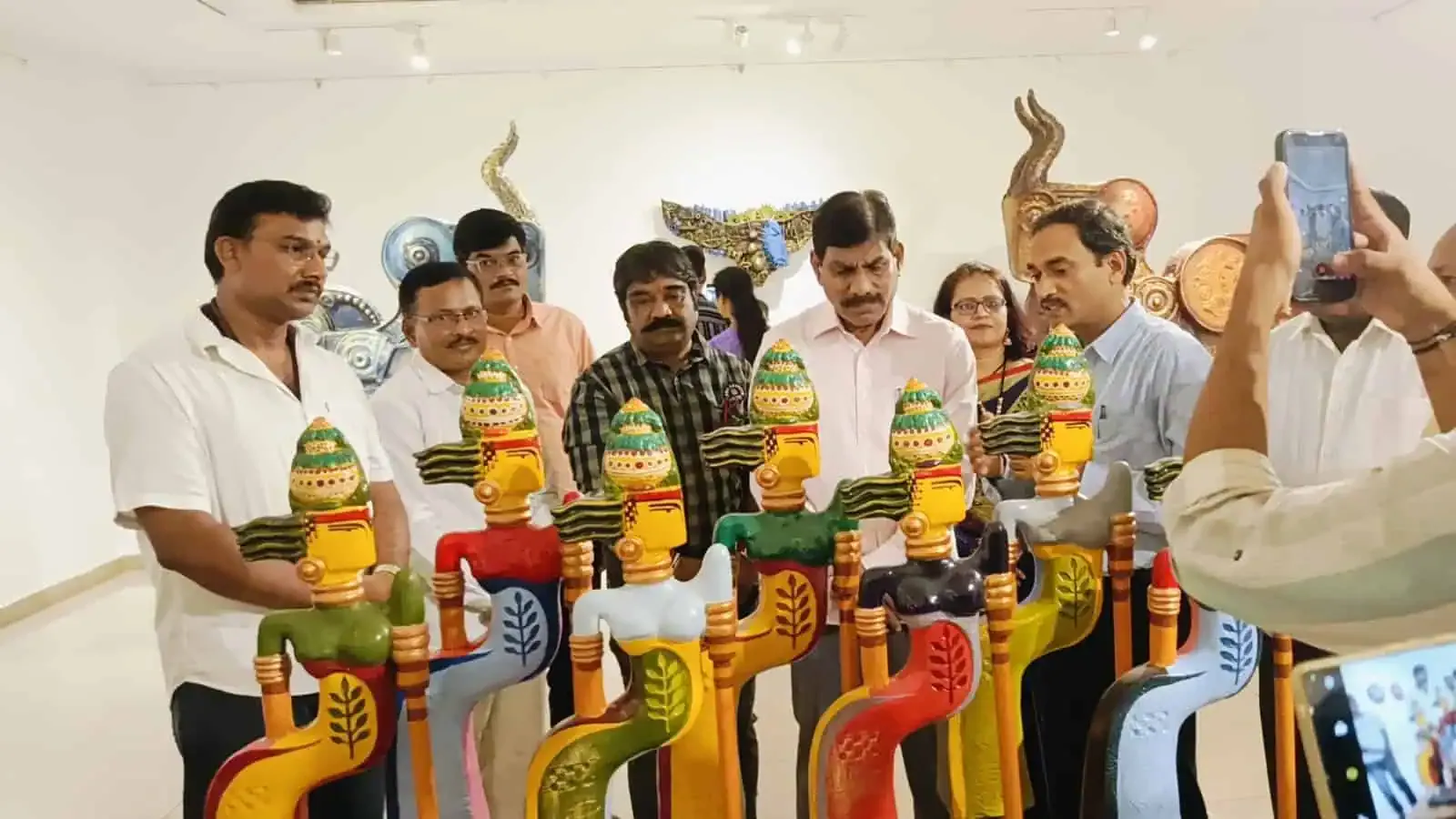 People holding painted wooden figures at an exhibition