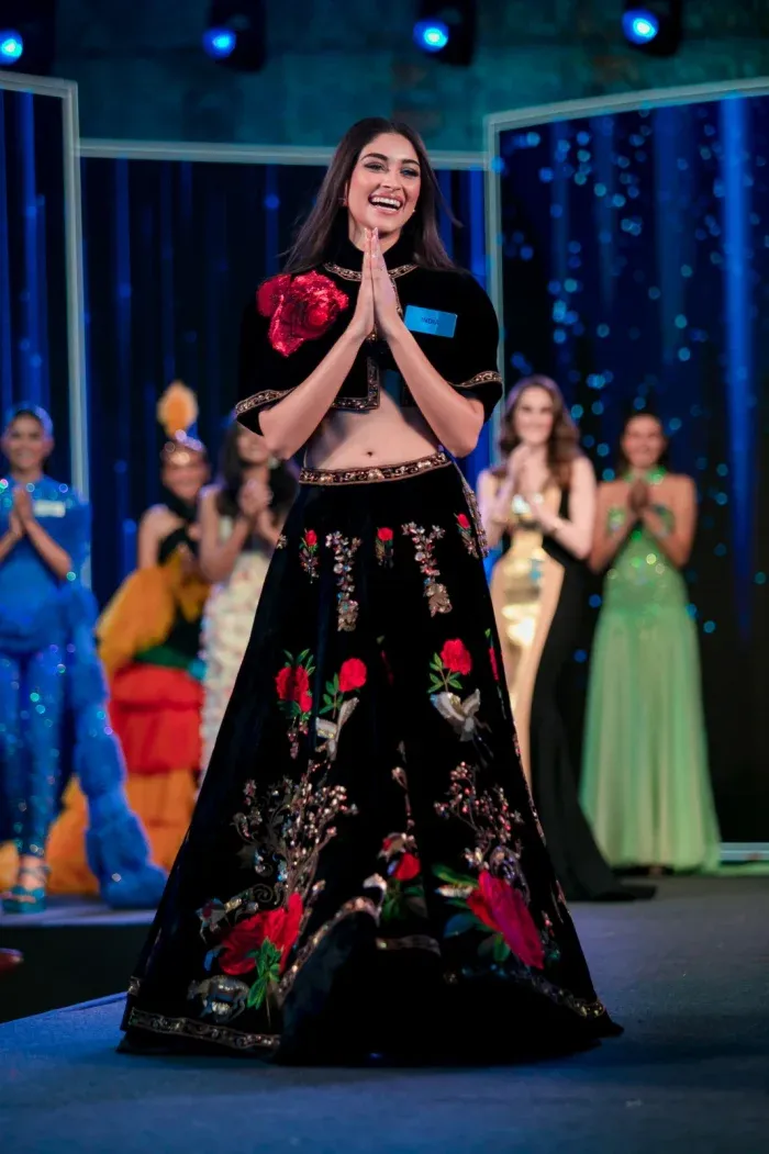 Woman in an embroidered outfit on a lit stage with others behind
