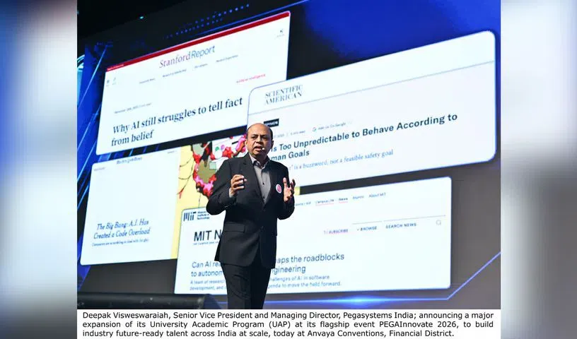 Man speaking on a stage beside a screen showing article headlines