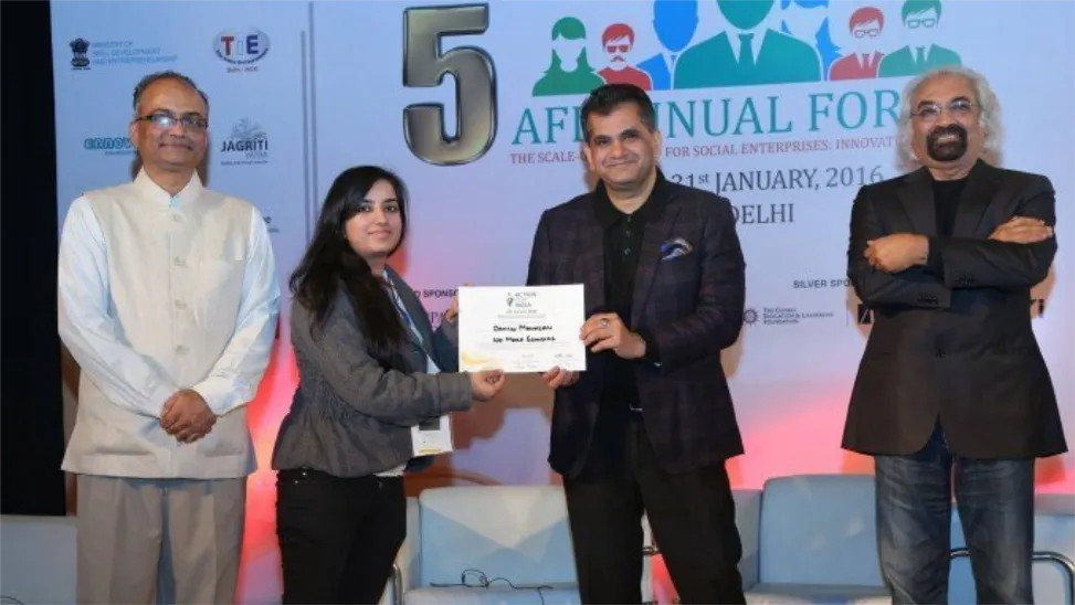 Four people on a stage, one handing a certificate to another, banner behind