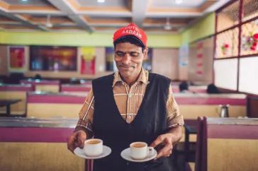 Man in a cap seated at a table with cups of tea